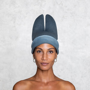 A woman from the shoulders up wearing a otton Knit Bat balaclava in faded indigo rolled up so her face is showing