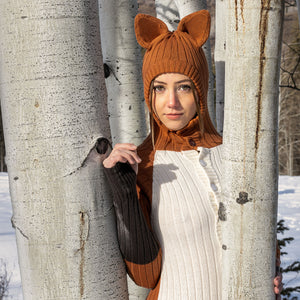 Person wearing a fox sweater with hooded ears between trees in a snowy forest