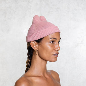 Woman from the chest up wearing a small pink beanie with little horns