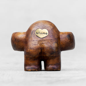 A rounded wooden figurine with a brass heart shaped emblem standing against a light gray background