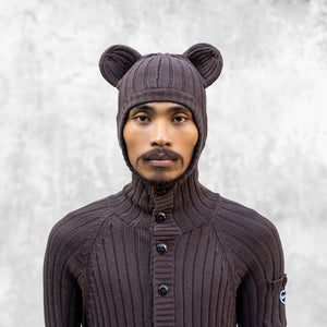 Person wearing a brown hooded knit sweater with bear ears against a light gray background