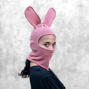 Person wearing a pink balaclava with bunny ears that covers their mouth against a light gray background