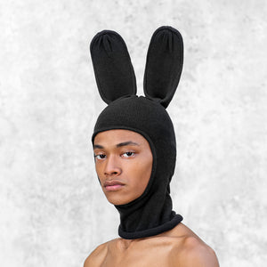 Person wearing a black balaclava with a face hole and tall bunny ears against a light gray background