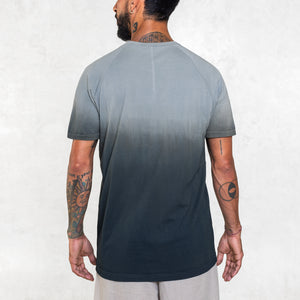 Man standing from the waist up facing back wearing a short sleeve cotton tee shirt that fades from indigo blue at the hem toward light blue at the shoulders