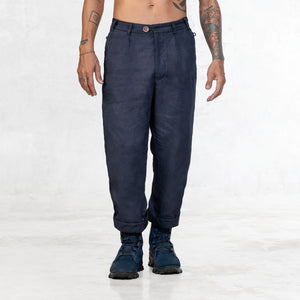 A shirtless man standing facing front from the waist down wearing Indigo blue linen pants and blue suede military style boots