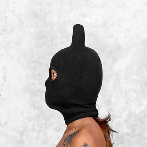 Person wearing a black balaclava with rounded ears with a light gray textured background