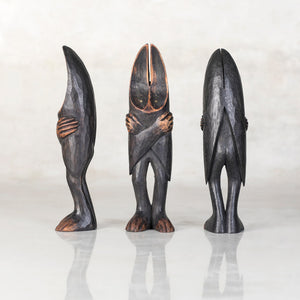 Three wooden bat sculptures with their hands crossed over their chest standing in different directions in front of a light gray background