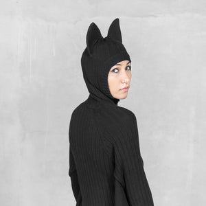Person wearing a black hooded sweater with pointed animal ears against a light gray background