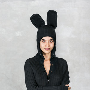 Person wearing a black hooded knit sweater with bunny rabbit ears against a gray background