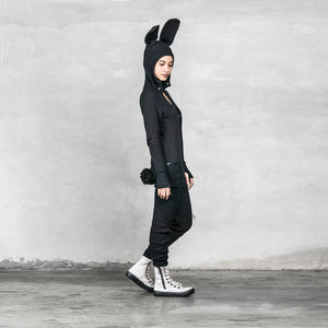 BLAMO Bunny Onesie Black, cotton knit with bunny ears and a tail, model is looking down while standing against a light gray textured background