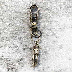 Brass monkey figurine keychain attached to a spring clip laying against a gray background