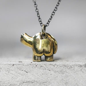 A brass rounded character charm pendant with one arm raised on a chain standing on a concrete ledge
