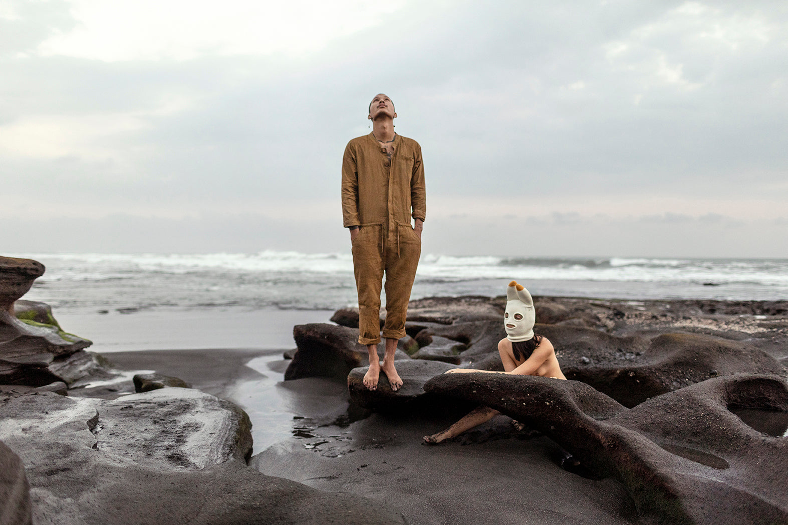 a man standing in a golden yellow jumpsuit on a black sand beach
