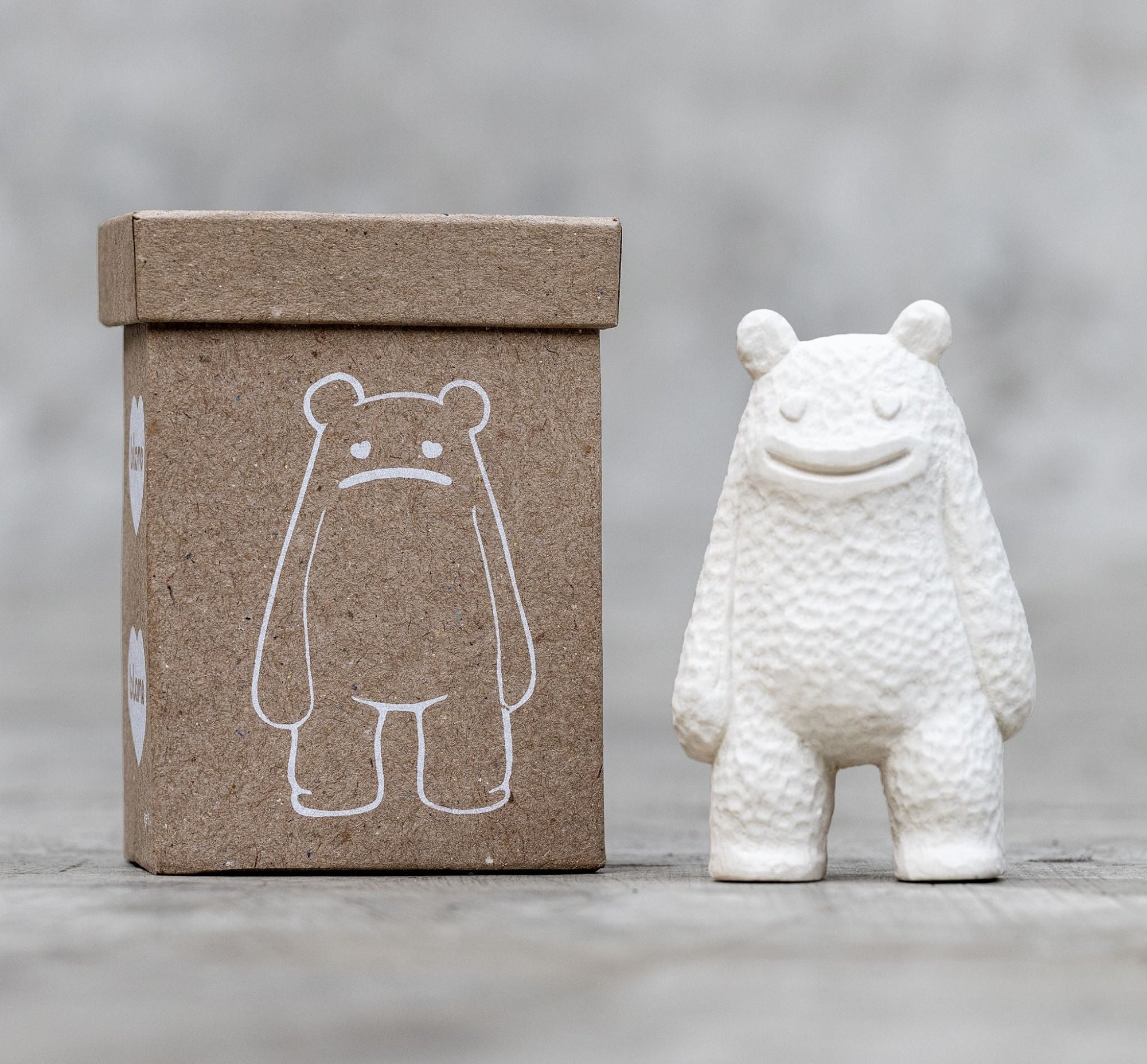 White textured ceramic bear figurine standing beside a brown kraft box printed with a simple bear illustration.