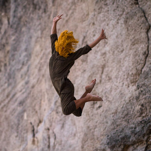 Person with yellow hair in a black outfit leaping against a rocky cliff.