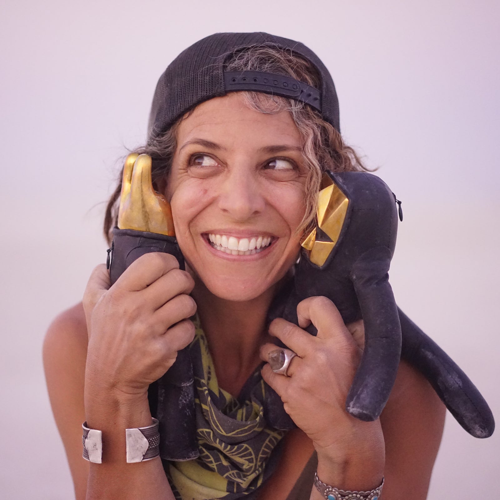 Person smiling holding two leather figurines up next to their face against a light gray bakground