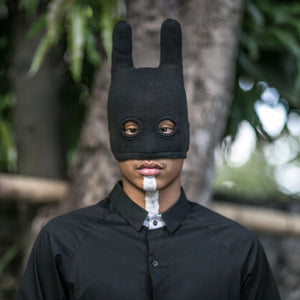 Person wearing a black bunny mask outdoors with trees in the background