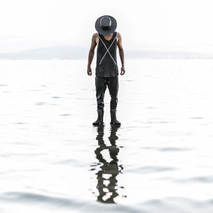 Person standing in water wearing a black outfit and hat, with a minimalistic design.