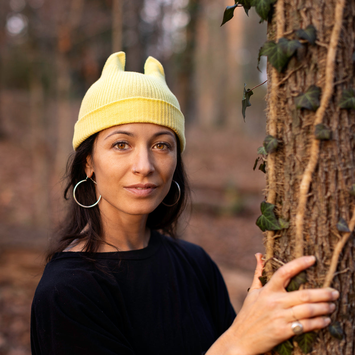 Person wearing a yellow knitted hat with animal ears, standing in a forest.