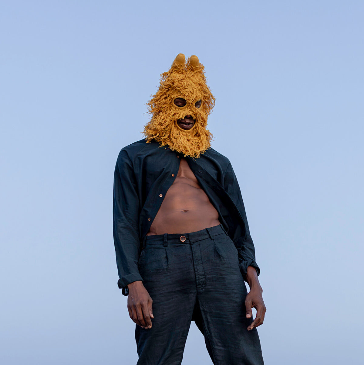 Person wearing a hairy mango mask and dark clothing against a blue background
