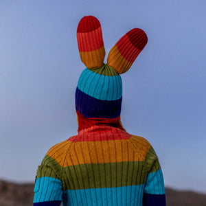 Person wearing a colorful striped sweater with bunny ears against a clear blue sky.
