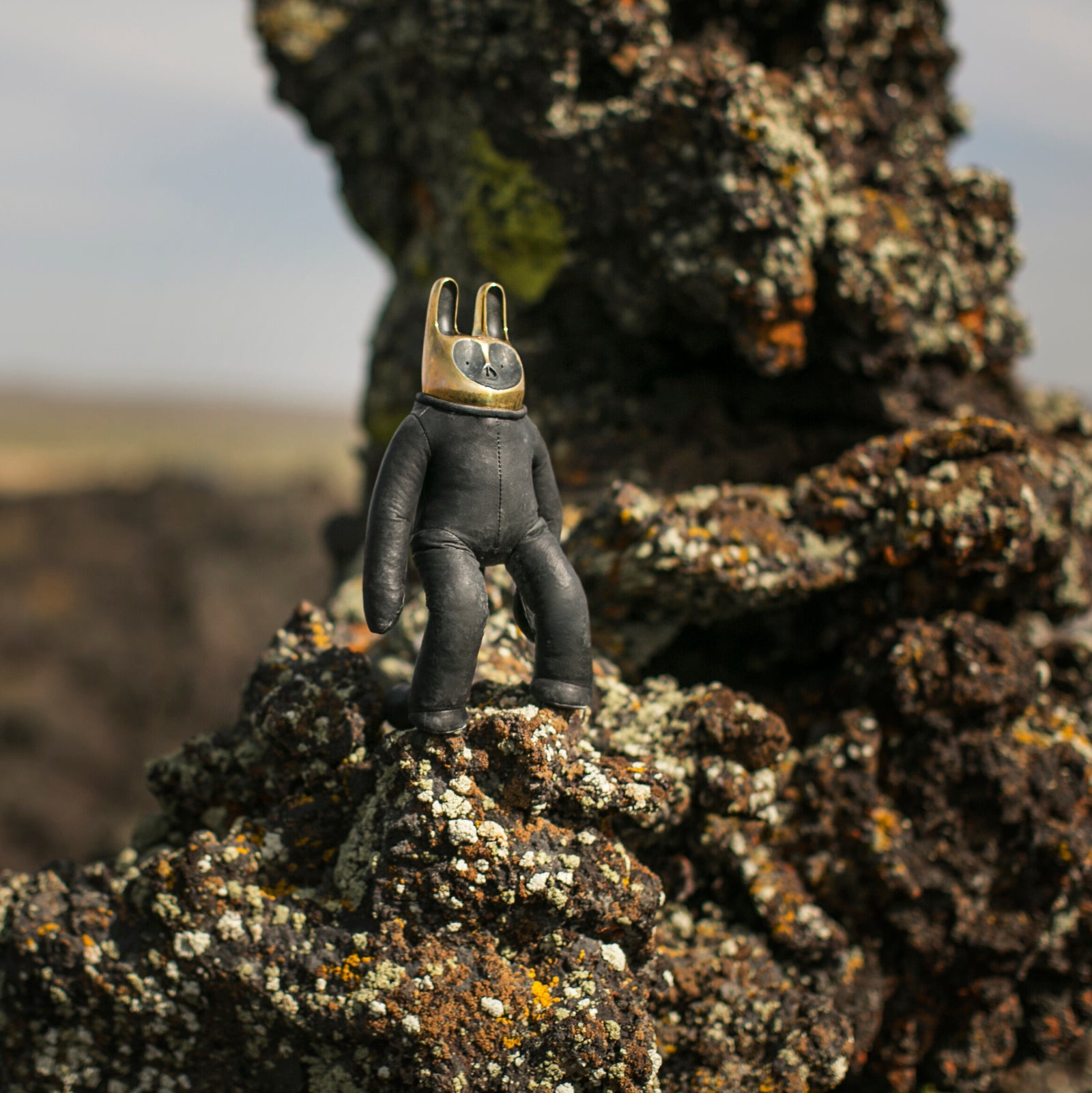 Leather figure with a golden brass head standing on a rocky surface.