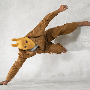 Person wearing a mango mask and tan jumpsuit pushing themself off the ground against a light gray background 