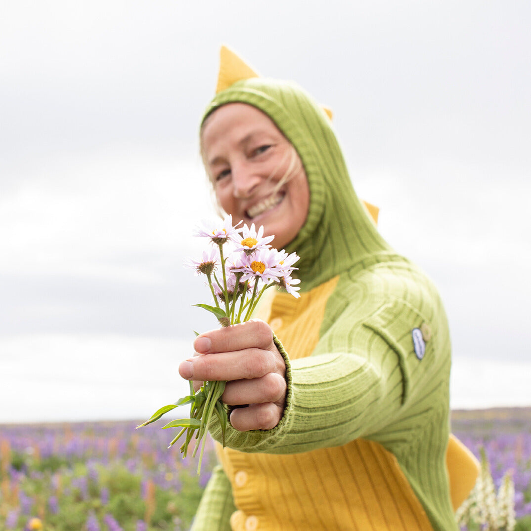 Person wearing a green dinosaur hoodie holding flowers in a field