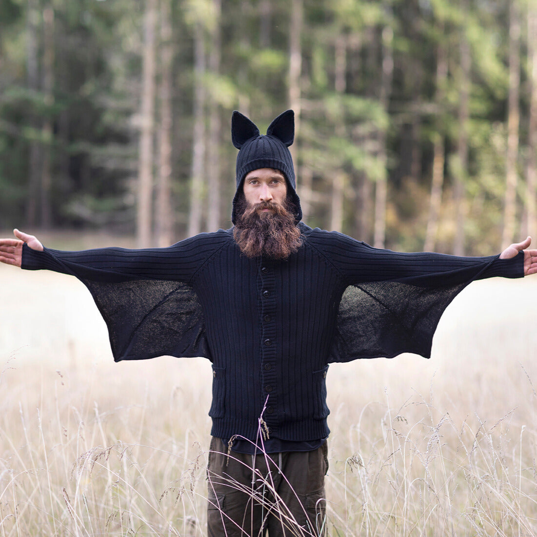 Person wearing a black knit sweater with bat ears and wings in a forest setting