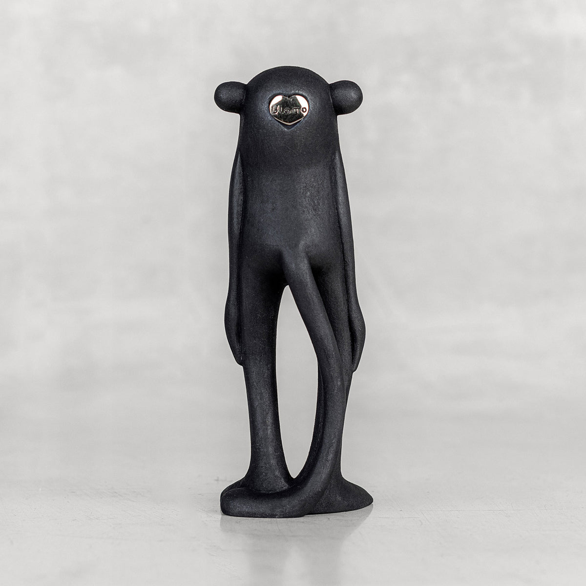 Back view of a black monkey figurine with a silver heart emblem on a white background