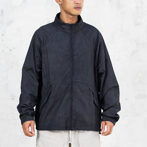 Person wearing a black zip up nylon mock neck jacket with sloped pockets standing in front of a light gray background 