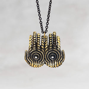 A close-up of a necklace featuring a double hand pendant with a textured gold finish and black enamel details, suspended on a black chain against a light gray background.