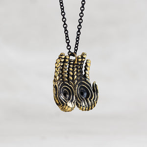 A necklace featuring a pendant with two hands with a textured gold finish and black enamel details, suspended on a black chain against a light gray background.