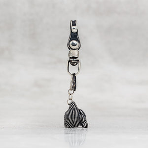 A silver-toned metal snap hook clasp with a dangling charm, shown against a light gray textured background.