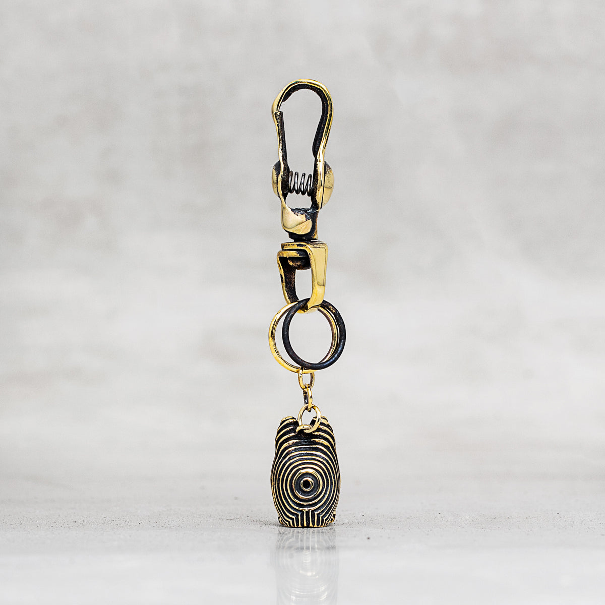 A gold and black metal keychain or bag charm with a lobster clasp, split ring, and a dangling pendant, shown on a light gray marble surface.