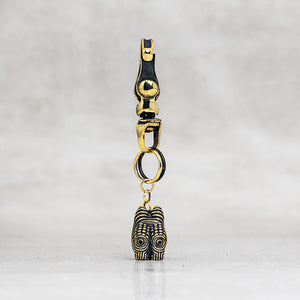 A gold and black metal accessory with a lobster clasp, jump ring, and a dangling charm, photographed against a light gray marble background.