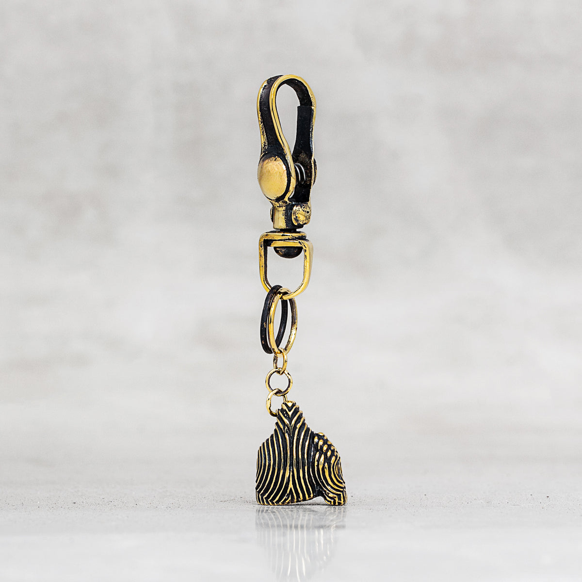 A gold-toned lobster clasp keychain or bag charm with a small dangling ornament, shown on a light gray marble-like background.