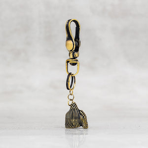 A gold-toned lobster clasp keychain or bag charm with a small dangling ornament, shown on a light gray marble-like background.