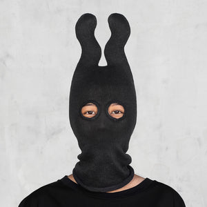 Person wearing a black knit balaclava with wavy horns and the top of the head and eyeholes against a light gray background