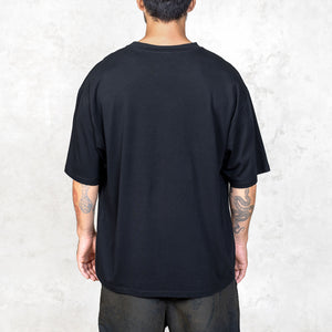 A tattooed person from the waist up facing back wearing a boxy cut black short sleeve tee. 