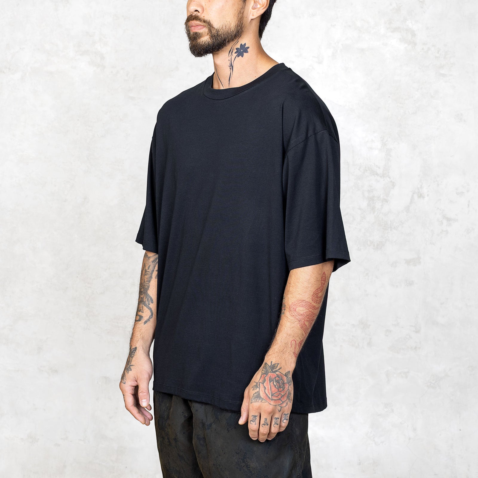 A tattooed person from the waist up wearing a boxy cut black short sleeve tee.
