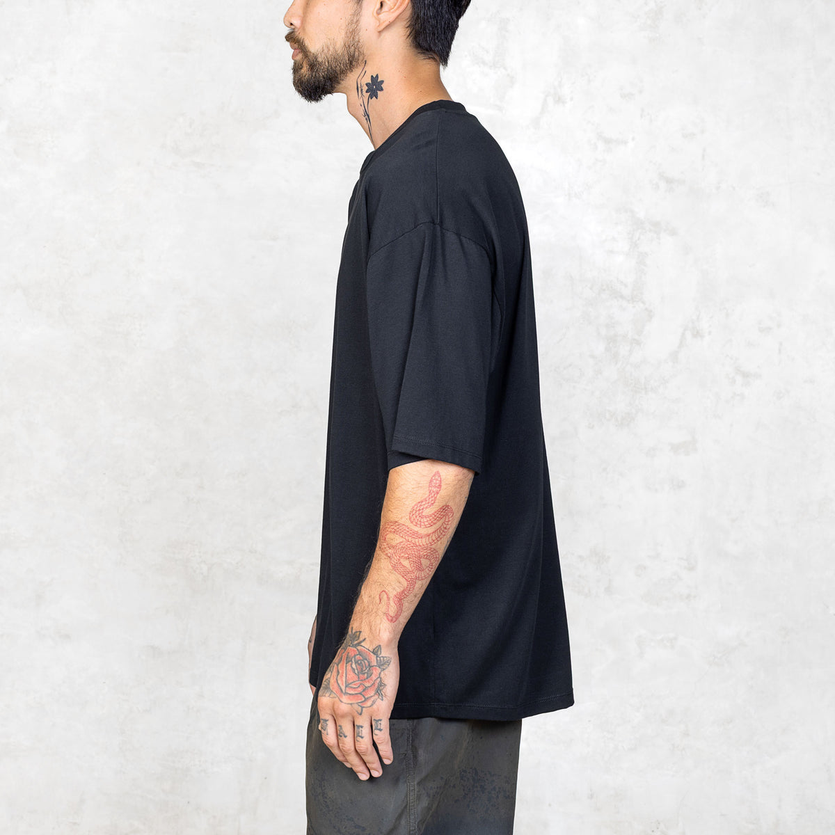 A person from the waist up facing sideways wearing a boxy cut black short sleeve tee.