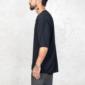 A person from the waist up facing sideways wearing a boxy cut black short sleeve tee. 