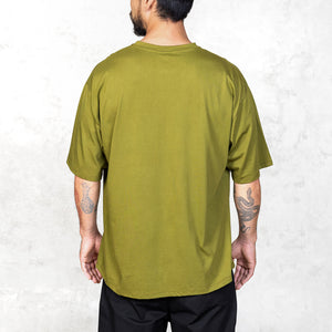 Tattooed person facing backwards wearing an oversized green t-shirt against a light gray background