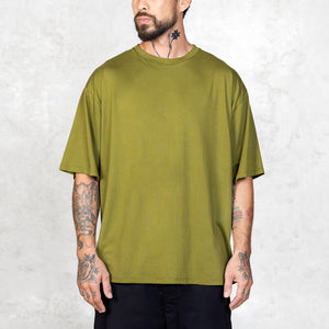Tattooed person facing forward wearing an oversized green t-shirt against a light gray background