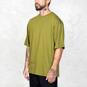 Tattooed person at an angle wearing an oversized green t-shirt against a light gray background