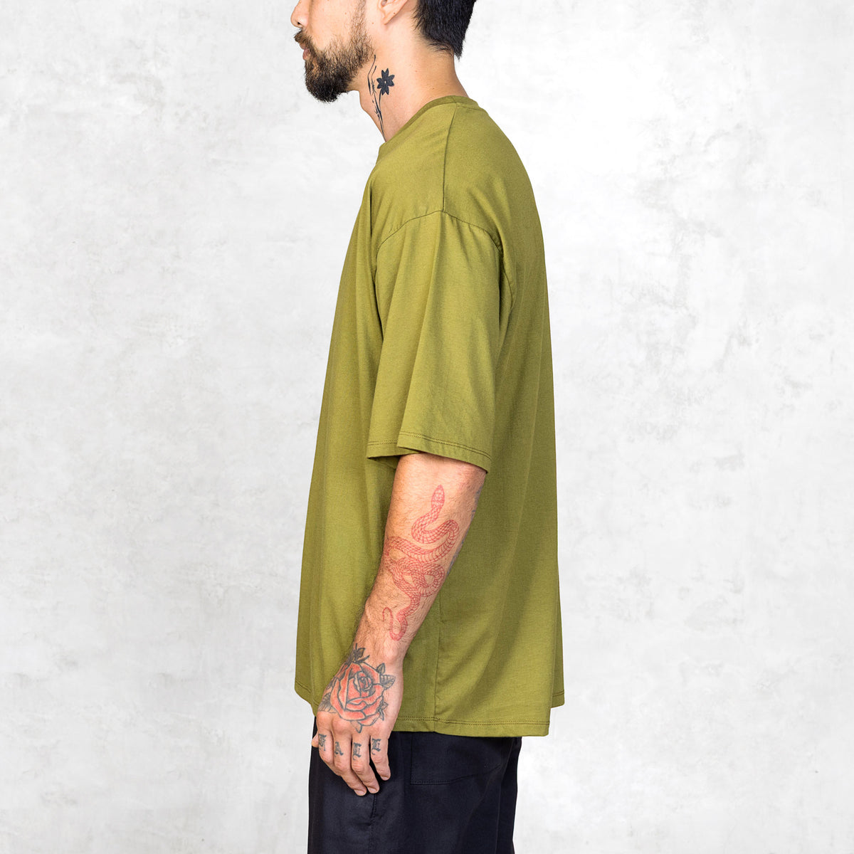 Tattooed person facing to the side wearing an oversized green t-shirt against a light gray background