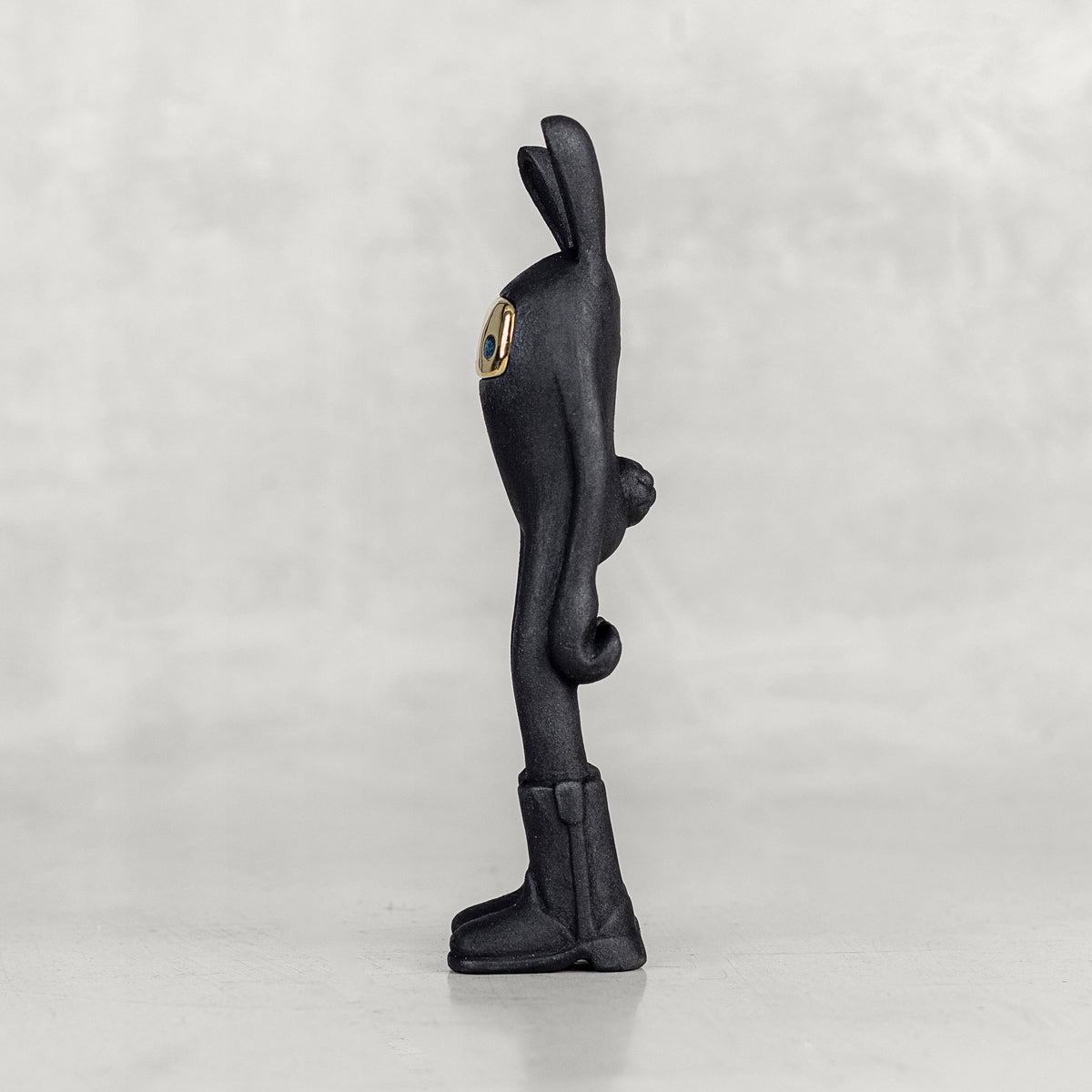Side view of a black bunny figure with a brass face on a white background