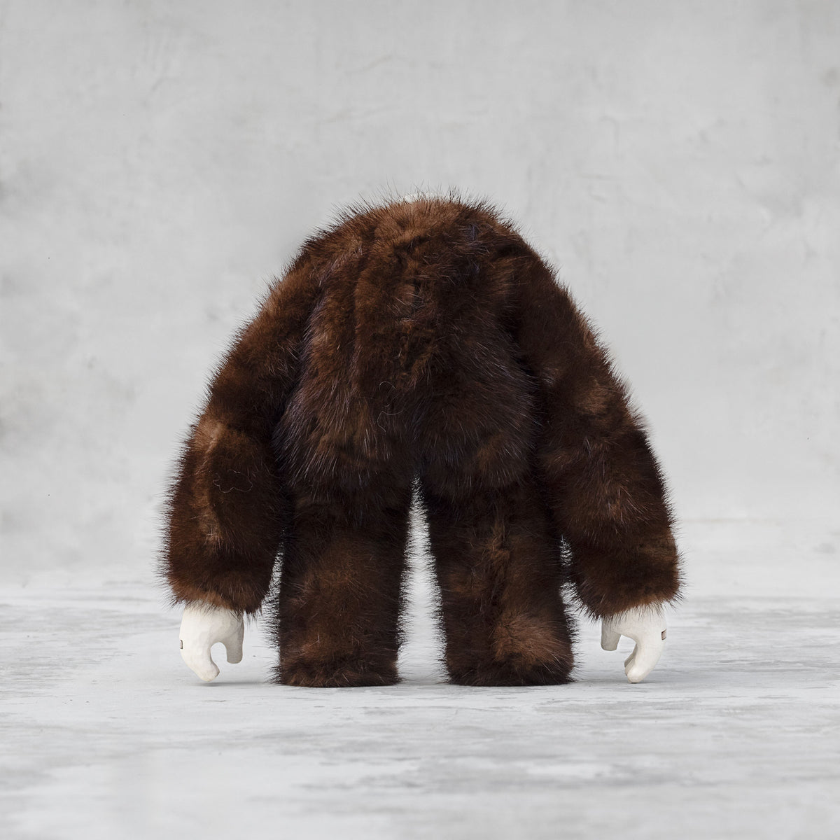 Back view of a ceramic, fur, and brass figurine standing against a light gray background