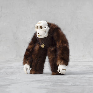 Quarter view of a ceramic, fur, and brass monkey skull figurine standing against a light gray background